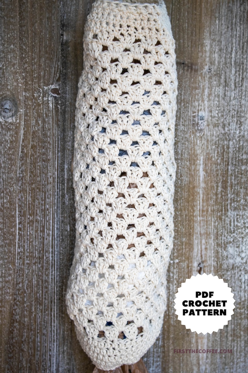 May include: A crocheted bag for storing plastic bags, hanging on a wooden wall. The bag is made with a white yarn and has a simple, open-stitch pattern. The text "PDF CROCHET PATTERN" is on a black circle with white stars.