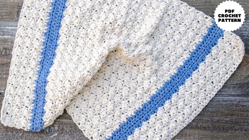 May include: A crocheted blanket with a blue stripe down the center. The blanket is made with a textured stitch and is a light cream color.