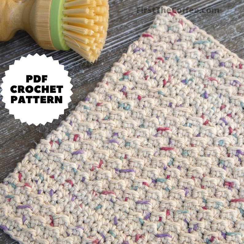 May include: A close-up of a crocheted dishcloth with a beige background and colorful flecks of yarn in pink, purple, and blue. The dishcloth is made with a simple stitch pattern and has a slightly textured surface. The text "PDF CROCHET PATTERN" is visible in the image.