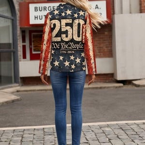 以下が含まれることがあります： 背中に「250 We The People 1776-2026」の文字が入った愛国的なデザインのブレザー。ブレザーは、白い星と赤と白のストライプが入ったネイビーブルーの背景です。その人は青いジーンズと濃い青色のハイヒールを履いています。