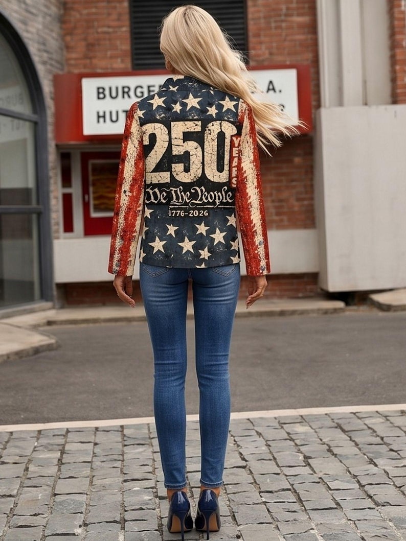 以下が含まれることがあります： 背中に「250 We The People 1776-2026」の文字が入った愛国的なデザインのブレザー。ブレザーは、白い星と赤と白のストライプが入ったネイビーブルーの背景です。その人は青いジーンズと濃い青色のハイヒールを履いています。