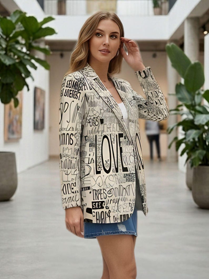 Puede incluir: Blazer color crema con texto negro y la palabra "LOVE" en un lugar destacado. El blazer tiene solapas con muescas y mangas largas. La modelo lleva un top blanco y pantalones cortos vaqueros.