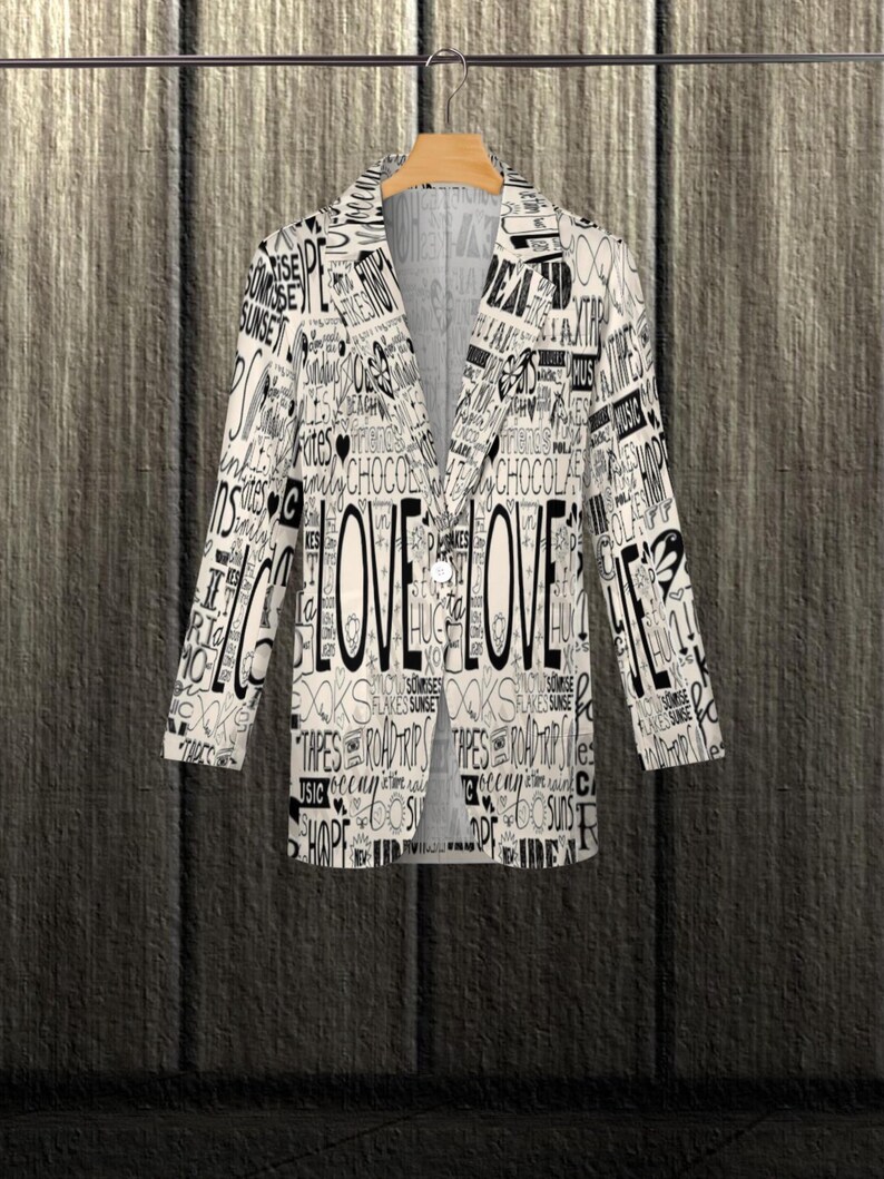 Puede incluir: Una blazer blanca con un dise&ntilde;o de palabras en negro, incluyendo la palabra "LOVE" en un lugar destacado. La blazer est&aacute; colgada en una percha de madera sobre un fondo de madera texturizada. El dise&ntilde;o incluye palabras como "SUNRISE" y "CHOCOLATE".
