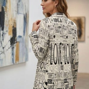 Puede incluir: Blazer color crema con un dise&ntilde;o de texto negro, incluyendo la palabra "LOVE" en letras grandes. El blazer se lleva con vaqueros azules. El fondo incluye arte abstracto y un entorno de galer&iacute;a.