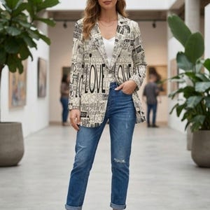 Puede incluir: Una mujer con una blazer crema con un dise&ntilde;o de texto negro, incluyendo la palabra "LOVE". Tambi&eacute;n lleva vaqueros azules y tacones dorados. La blazer tiene cuello y mangas largas. Los vaqueros tienen un aspecto desgastado.