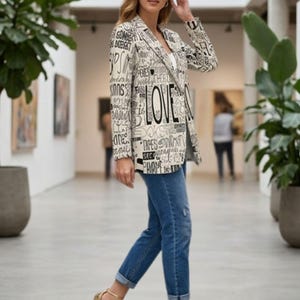 Puede incluir: Una blazer crema con texto negro, incluyendo la palabra "LOVE", combinada con vaqueros azules y tacones dorados. El conjunto se luce en un pasillo luminoso con plantas.