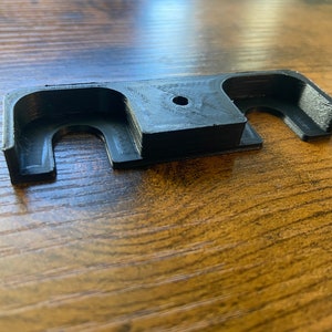 May include: A black plastic tool with two holes and a small round hole in the center. The tool is designed to help with the installation or removal of something.