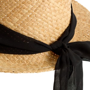 May include: A straw hat with a wide brim and a black ribbon tied around it. The ribbon is tied in a bow at the side of the hat.