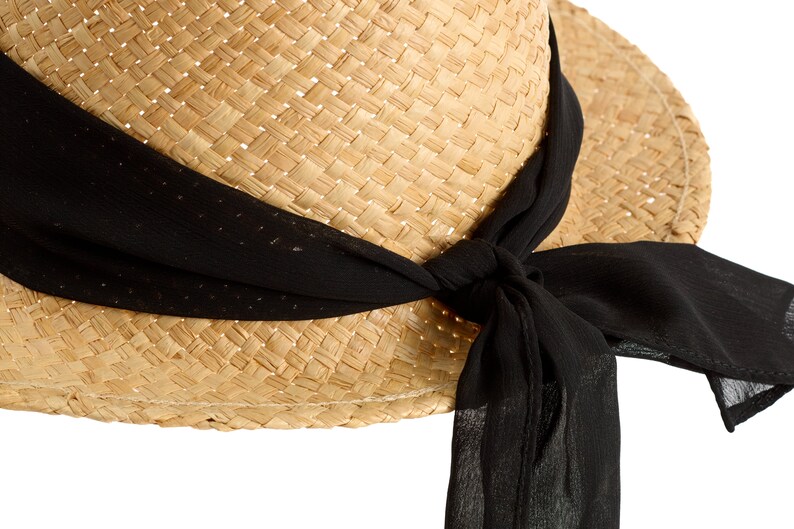 May include: A straw hat with a wide brim and a black ribbon tied around it. The ribbon is tied in a bow at the side of the hat.