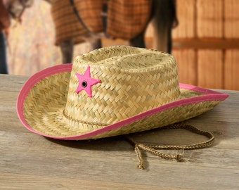 May include: A straw cowboy hat with a pink band and a pink star on the front. The hat is on a wooden surface.