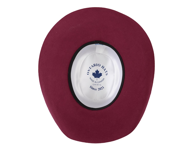 K&ouml;nnte beinhalten: Die Innenseite eines burgunderfarbenen Filzhutes mit einem schwarzen Band und einem wei&szlig;en Etikett mit der Aufschrift "Ontario Hats, Made in Canada, OAF 6619, Since 2021".