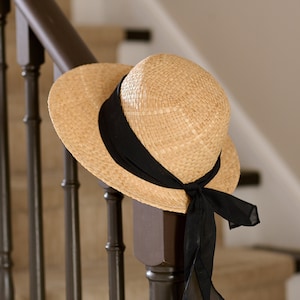 May include: A straw hat with a black ribbon and bow, hanging on a wooden railing.