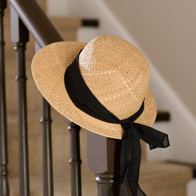 May include: A straw hat with a black ribbon and bow, hanging on a wooden railing.