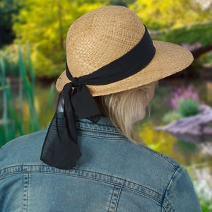 May include: A straw hat with a wide brim and a black ribbon tied around the crown. The ribbon is tied in a bow at the back of the hat.