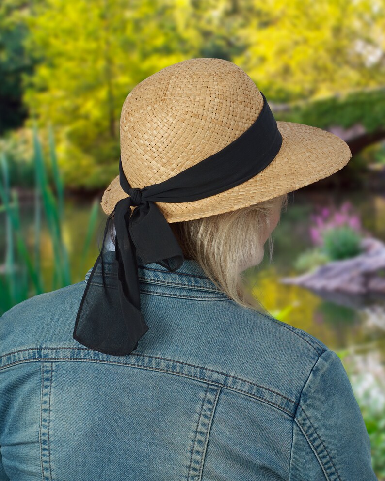 May include: A straw hat with a wide brim and a black ribbon tied around the crown. The ribbon is tied in a bow at the back of the hat.