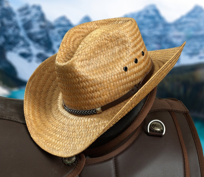 May include: A straw cowboy hat with a brown leather band and a brown leather saddle in the background.
