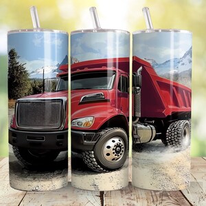 May include: A red dumper truck with a white cab and a black grille. The truck is driving on a dirt road with a mountain range in the background.