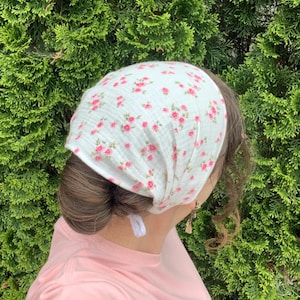 May include: A white headband with a pink floral pattern. The headband is tied in a knot at the back of the head.