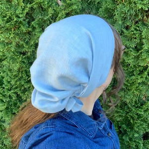 Pode incluir: Um len&ccedil;o de cabe&ccedil;a azul-claro feito de um tecido entrela&ccedil;ado com textura vis&iacute;vel. O len&ccedil;o &eacute; atado na parte de tr&aacute;s com um n&oacute; e cai suavemente sobre a cabe&ccedil;a, oferecendo uma cobertura total com um aspeto macio e franzido.