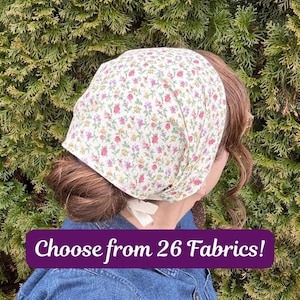 May include: A floral print head covering with a white background and small pink, yellow, and purple flowers. The text "Choose from 26 Fabrics!" is displayed in a purple box. The head covering is tied at the nape of the neck.
