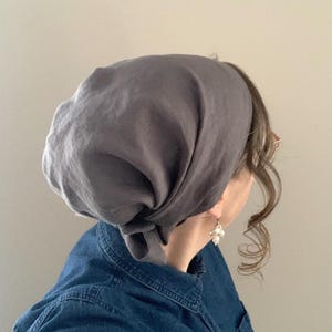 Pode incluir: Um len&ccedil;o de cabe&ccedil;a cinza-escuro s&oacute;lido atado na nuca, feito de um tecido macio e leve. O len&ccedil;o cobre o topo da cabe&ccedil;a com um ajuste solto e drapeado, apresentando um detalhe de n&oacute; simples na parte de tr&aacute;s e uma textura mate lisa.