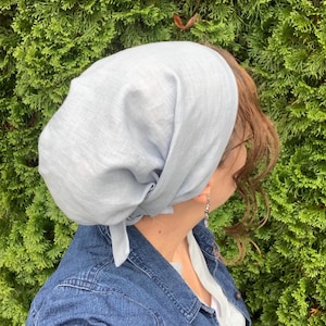 Pode incluir: Uma cobertura de cabe&ccedil;a azul-clara feita de um tecido macio e entrela&ccedil;ado, amarrada na parte de tr&aacute;s. O len&ccedil;o apresenta um ajuste solto e drapeado que cobre o cabelo completamente, com dobras vis&iacute;veis e um pequeno n&oacute; na nuca.