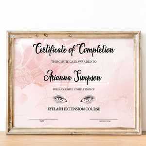 Peut inclure: Un certificat encadré avec un motif de marbre rose et doré. Le certificat indique "Certificat de réussite" et "Cours d'extension de cils". Le certificat est décerné à "Arianna Simpson".