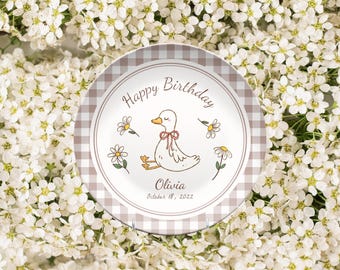 May include: A decorative plate with a duck illustration, daisies, and the text "Happy Birthday" in a circular design. The plate has a gingham border and includes the name "Olivia" and the date "October 18, 2022".