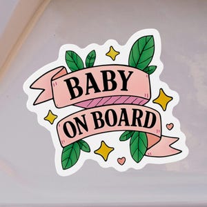 Baby On Board magnet with pink ribbon, stars, and green leaves on white car