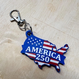 May include: A blue, red, and white keychain in the shape of the United States with the text "AMERICA 250". The keychain has a silver clasp and ring.