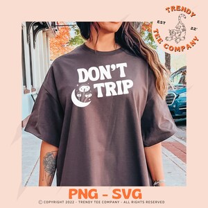 Könnte beinhalten: Ein dunkelgraues T-Shirt mit einem weißen Grafikdesign, auf dem "Don't Trip" mit einem Halbmond und Pilzen steht. Die Grafik ist im Retro-Stil gehalten.