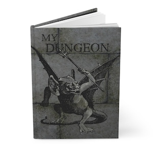 May include: A gray stone-textured journal cover with the text "MY DUNGEON" in black lettering. A black and white illustration of a gargoyle holding a trident is in the center of the cover.