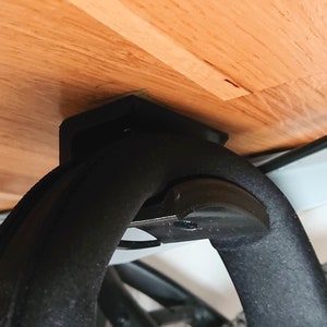以下が含まれることがあります： 木製の表面に取り付けられた黒い自転車ラックのクローズアップ。ラックには、自転車のフレームを保護するためのゴム製の腕があります。