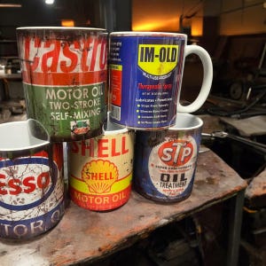 Puede incluir: Cuatro tazas de cerámica con diseños de latas de aceite de estilo vintage. Las tazas muestran los logotipos de Castrol, Im-Old, Shell y STP. Las tazas están apiladas, con la taza Castrol en la parte superior y la taza STP en la parte inferior.