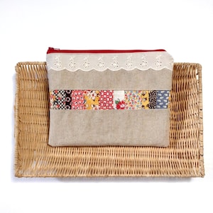 May include: A beige linen zippered pouch with a red zipper and white lace trim. The pouch has a patchwork design with colorful fabric squares.