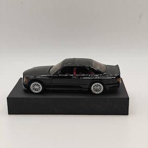 Pode incluir: Modelo de carro preto em metal fundido com interior vermelho e rodas prateadas. O carro está em uma base de exibição preta.