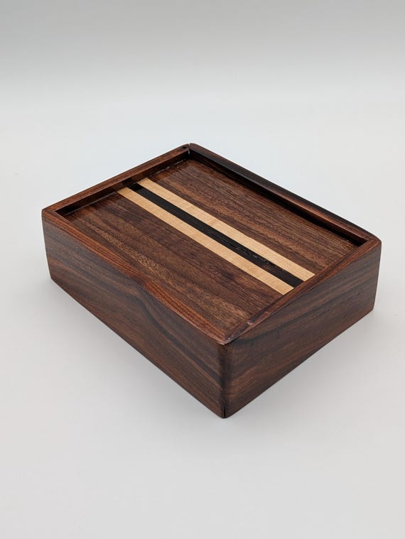 A three-wood sliding-lid box in walnut, ebony, and maple — the contrast grain pattern alone makes it a tiny piece of furniture worth keeping on a desk forever.