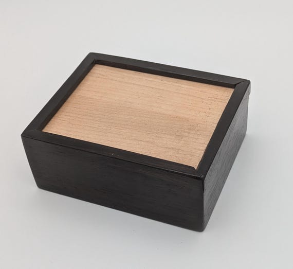 A hand-crafted sliding-lid box in contrasting ebony and maple — the two-tone wood joinery is genuinely striking and screams 'a skilled woodworker made this, not a factory.'