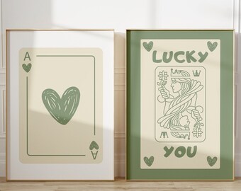 May include: Two framed prints with a green and cream color scheme. The left print features a green heart on a cream background with the letter A and a heart symbol in the top left corner. The right print features a green queen of hearts playing card with the text "LUCKY YOU" in the bottom center.