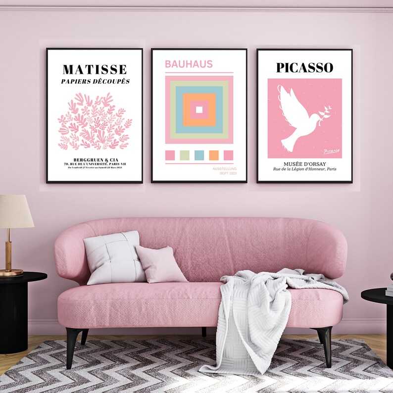 May include: Three framed art prints with pink backgrounds. The left print features a Matisse paper cut design with the text "MATISSE PAPIERS D&Eacute;COUP&Eacute;S". The middle print features a Bauhaus geometric design with the text "BAUHAUS". The right print features a Picasso dove design with the text "PICASSO" and "MUS&Eacute;E D'ORSAY".