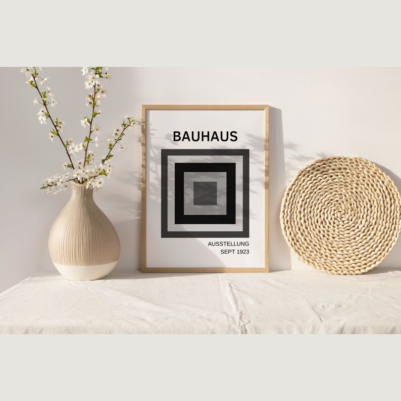 May include: A framed print with the word "BAUHHAUS" in black text and a black square with concentric gray squares inside. The text "AUSSTELLUNG SEPT 1923" is below the square.