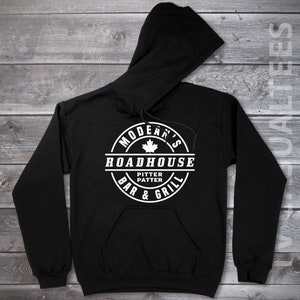 May include: Black hooded sweatshirt with a white circular logo that says "Modean's Roadhouse Bar & Grill" with a maple leaf and the words "Pitter Patter" inside.