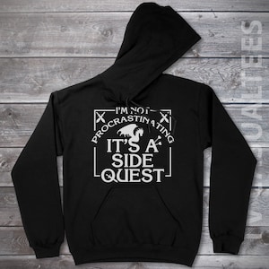 May include: Black hooded sweatshirt with a white graphic print that says "I'm not procrastinating, it's a side quest." The graphic also includes a dragon and a sword.
