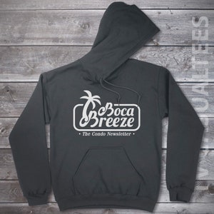 May include: A dark gray hooded sweatshirt with a white graphic design of a palm tree and the text "Boca Breeze - The Condo Newsletter".
