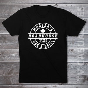 May include: Black t-shirt with a white circular logo that says "Modean's Roadhouse Bar & Grill" with a Canadian maple leaf and the words "Pitter Patter" inside.