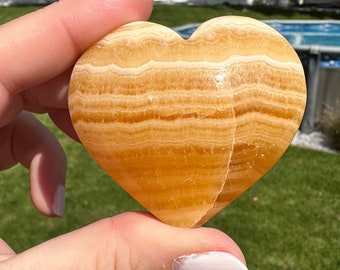 May include: A heart-shaped, polished, orange and white banded calcite crystal.