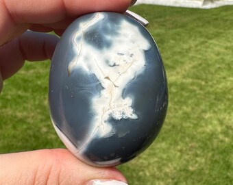 May include: A smooth, gray and white agate egg with a swirling pattern. The egg is being held in a hand.