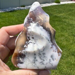 May include: A white, brown, and purple agate stone with a flame-like shape. The stone has a natural, rough texture and is a unique piece of nature.