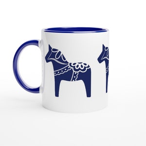 May include: White ceramic mug with a blue rim and handle. The mug features a repeating pattern of blue stylized horses with white details.