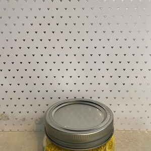 May include: A glass jar with a silver lid filled with yellow nutritional yeast flakes.